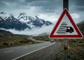 O que significa a placa de trânsito com triângulo de bordas vermelhas e um carro atravessado por listras?