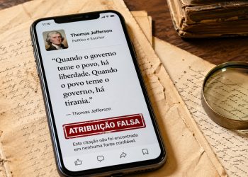 Celular mostra citação política com aviso de atribuição falsa ao lado de documentos antigos.