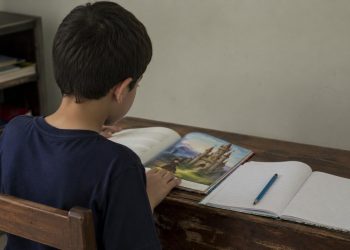 Criança lê um livro de contos de fadas em uma mesa de estudo.