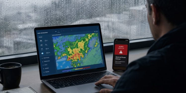 Pessoa consulta dados ambientais e alerta público durante chuva forte.