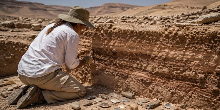 Arqueólogo examina camadas antigas e ferramentas de pedra em sítio que revela adaptação humana ao clima extremo.