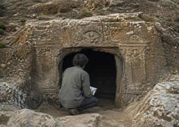 Arqueólogo observa a entrada de uma tumba pré-histórica escavada na rocha na Sardenha.
