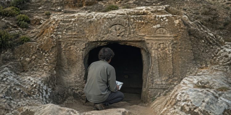 Arqueólogo observa a entrada de uma tumba pré-histórica escavada na rocha na Sardenha.