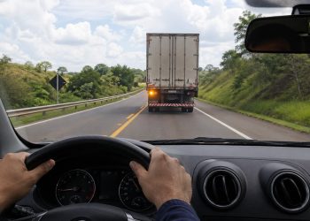 Motorista reduz a velocidade ao perceber o alerta luminoso de um caminhão na estrada.