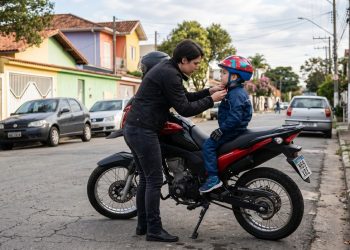 Adulto ajusta o capacete infantil antes de transportar a criança na garupa da moto.