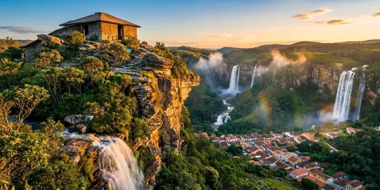 Vista panorâmica de cidade histórica cercada por cachoeiras, vegetação verde e formações rochosas ao pôr do sol.