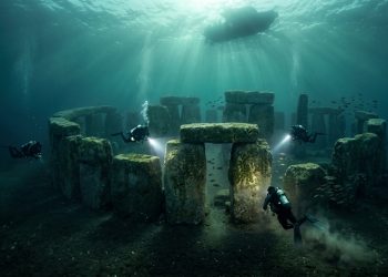 Mergulhadores exploram estruturas de pedra submersas semelhantes a monumentos antigos, iluminadas por feixes de luz vindos da superfície.