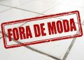 Carimbo vermelho com a expressão 'FORA DE MODA' aplicado sobre um piso antigo de cerâmica branca com rejunte escuro e desgastado.