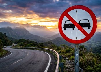 Sinalização de trânsito orienta motoristas em trecho de serra com pista sinuosa e baixa visibilidade.