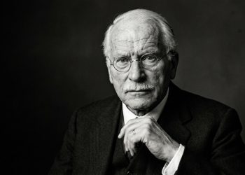 Homem idoso de óculos aparece em retrato preto e branco, com expressão séria e mão apoiada sob o queixo.