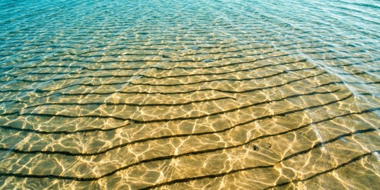 Ondulações douradas aparecem no fundo raso do mar cristalino