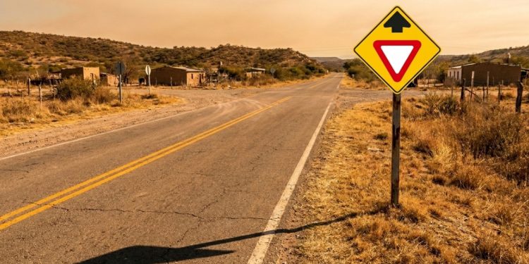 Placa triangular com seta preta avisa cruzamento em estrada latina
