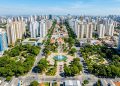 Vista aérea de bairro urbano planejado, com prédios altos, avenidas largas, praça central com fonte e áreas verdes.