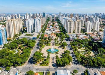 Vista aérea de bairro urbano planejado, com prédios altos, avenidas largas, praça central com fonte e áreas verdes.