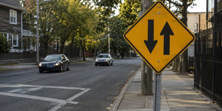 O que significa a placa de trânsito com duas setas pretas verticais paralelas apontando para sentidos opostos?