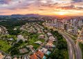 Vista aérea panorâmica de Valinhos, em São Paulo, com bairros residenciais, áreas verdes, avenidas, prédios e pôr do sol ao fundo.