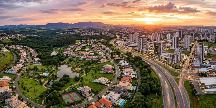 Vista aérea panorâmica de Valinhos, em São Paulo, com bairros residenciais, áreas verdes, avenidas, prédios e pôr do sol ao fundo.