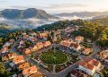 Vista aérea de Nova Petrópolis, na Serra Gaúcha, com casas de estilo europeu, igreja, labirinto verde e montanhas ao fundo.