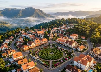 Vista aérea de Nova Petrópolis, na Serra Gaúcha, com casas de estilo europeu, igreja, labirinto verde e montanhas ao fundo.