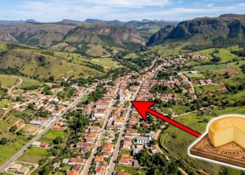 Vista aérea da cidade de São Roque de Minas cercada pelas montanhas verdes da Serra da Canastra, com uma intervenção gráfica mostrando um queijo artesanal no canto inferior direito e uma grossa seta vermelha apontando para a igreja matriz no centro da cidade.