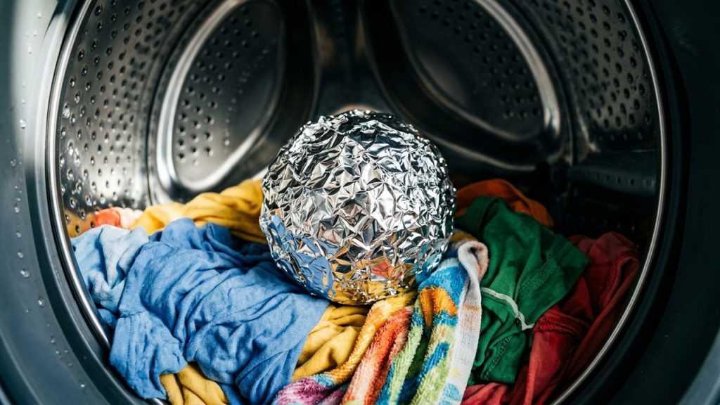 Bola de papel-alumínio sobre roupas coloridas dentro do tambor da máquina de lavar, em cena associada a dicas de lavanderia.