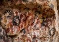 Pinturas rupestres com marcas de mãos coloridas em parede de caverna, representando arte pré-histórica.