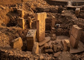 Representação de escavação arqueológica em Göbekli Tepe, na Turquia, com pilares de pedra esculpidos e estruturas circulares antigas.