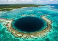 Vista aérea de um buraco azul em lagoa tropical, cercado por águas cristalinas, recifes e vegetação costeira.