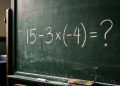 Quadro escolar com a expressão matemática 15 - 3 x (-4) = ? escrita em giz branco.