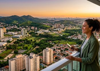 Mulher observa cidade arborizada do alto de uma varanda, com prédios, bairros residenciais, áreas verdes e pôr do sol ao fundo.