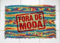 Tapete de crochê colorido sobre piso branco aparece com carimbo vermelho com a frase “Fora de moda”.