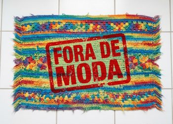 Tapete de crochê colorido sobre piso branco aparece com carimbo vermelho com a frase “Fora de moda”.