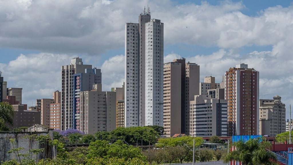 Vista urbana de Curitiba com prédios altos, áreas verdes e céu parcialmente nublado.