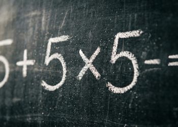 Expressão matemática 5 + 5 × 5 = ? escrita com giz branco em uma lousa escura, destacando uma conta simples que depende da ordem das operações.