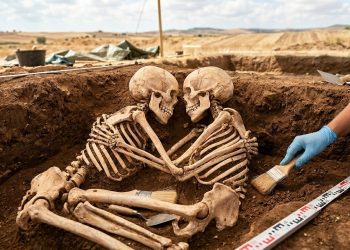 Dois esqueletos humanos aparecem lado a lado em uma escavação arqueológica, posicionados frente a frente em uma sepultura antiga.