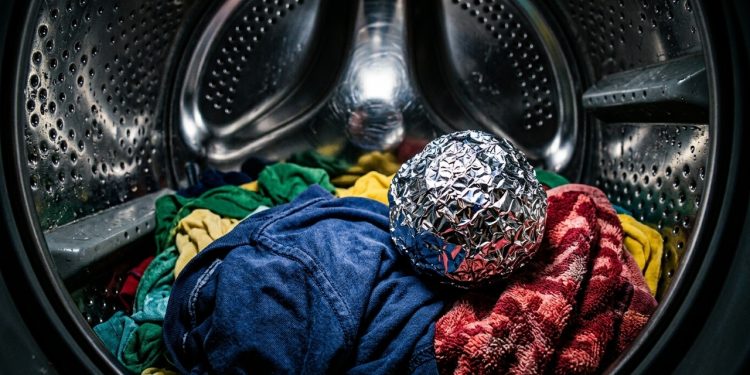 Bola de papel-alumínio sobre roupas coloridas dentro de máquina de lavar, em cena associada a truques de lavanderia.