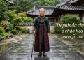 Pessoa idosa em traje tradicional em pátio de arquitetura coreana, ao lado da frase “Depois da chuva, o chão fica mais firme”.