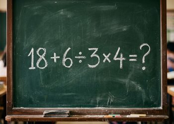 Quadro verde em sala de aula com a expressão matemática 18 + 6 ÷ 3 × 4 = ? escrita em giz branco.