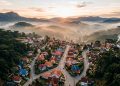 Vista aérea de Monte Verde, em Minas Gerais, com casas em meio à vegetação, ruas sinuosas, montanhas e neblina ao amanhecer.