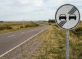 O que significa a placa de trânsito com dois carros juntos em um fundo branco e quatro linhas diagonais?