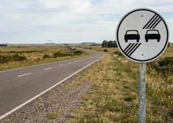 O que significa a placa de trânsito com dois carros juntos em um fundo branco e quatro linhas diagonais?