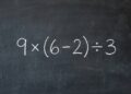 Visão frontal detalhada de um quadro-negro escolar tradicional. Bem no centro, a expressão matemática 9 \(6 - 2) \3 está escrita em giz branco de forma bastante nítida. O fundo escuro da lousa apresenta leves manchas e texturas de pó de giz previamente apagado.
