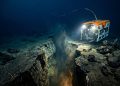 Veículo submarino operado remotamente ilumina uma fenda no fundo do oceano, com rochas, sedimentos e atividade geológica em águas profundas.