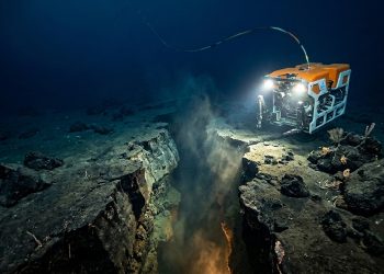 Veículo submarino operado remotamente ilumina uma fenda no fundo do oceano, com rochas, sedimentos e atividade geológica em águas profundas.