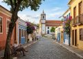 Rua histórica de Santana de Parnaíba, com casarões coloridos, calçamento de pedra, igreja ao fundo e pessoas caminhando em ambiente tranquilo.