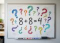Lousa branca fixada na parede de uma sala de aula com a equação matemática 8 + 8 = 4 escrita no centro com marcador preto. A equação está cercada por diversos pontos de interrogação desenhados em cores variadas, como azul, vermelho, verde e amarelo. Na calha da lousa há três canetas marcadoras e um apagador.