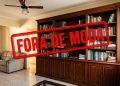 Sala de estar com estante de livros e móveis de madeira, marcada por um grande selo vermelho com a frase “Fora de moda”.